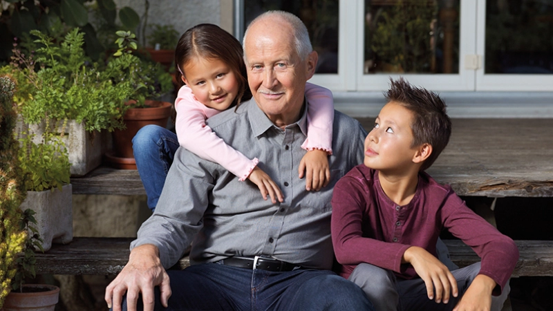 Un senior est assis avec ses deux petits-enfants sur les marches dans le jardin