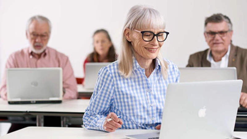Une femme âgée portant des lunettes est assise devant son ordinateur dans son bureau.
