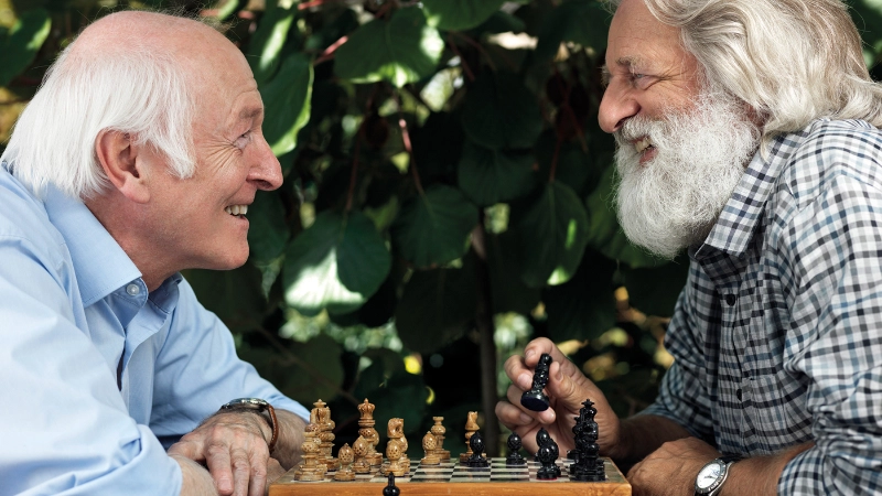 Deux hommes âgés jouent aux échecs et rient ensemble.