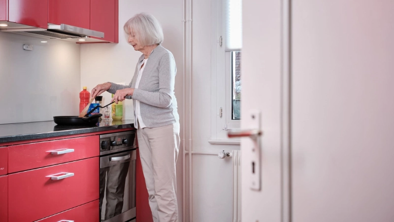 Une dame âgée debout devant la cuisinière dans la cuisine