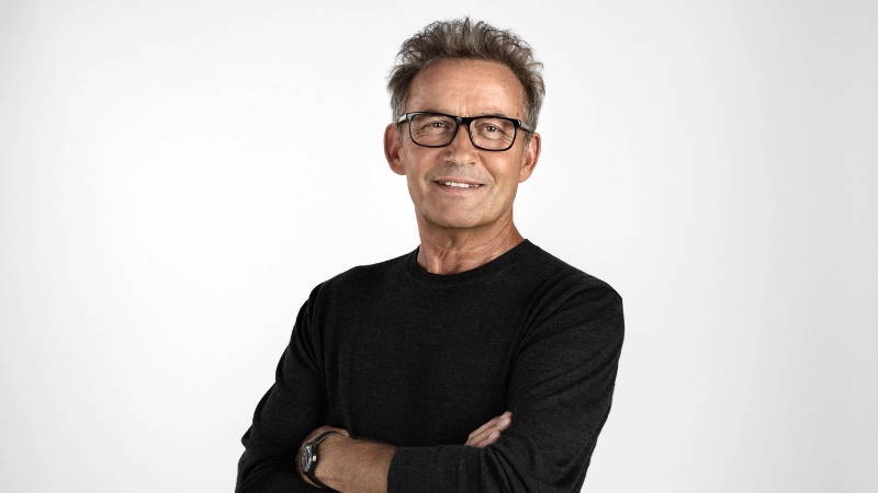 Homme âgé, bras croisés, lunettes, souriant.