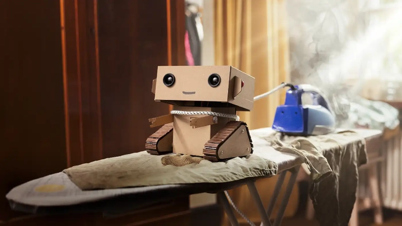 Le robot en carton Robi essaie de repasser des vêtements.