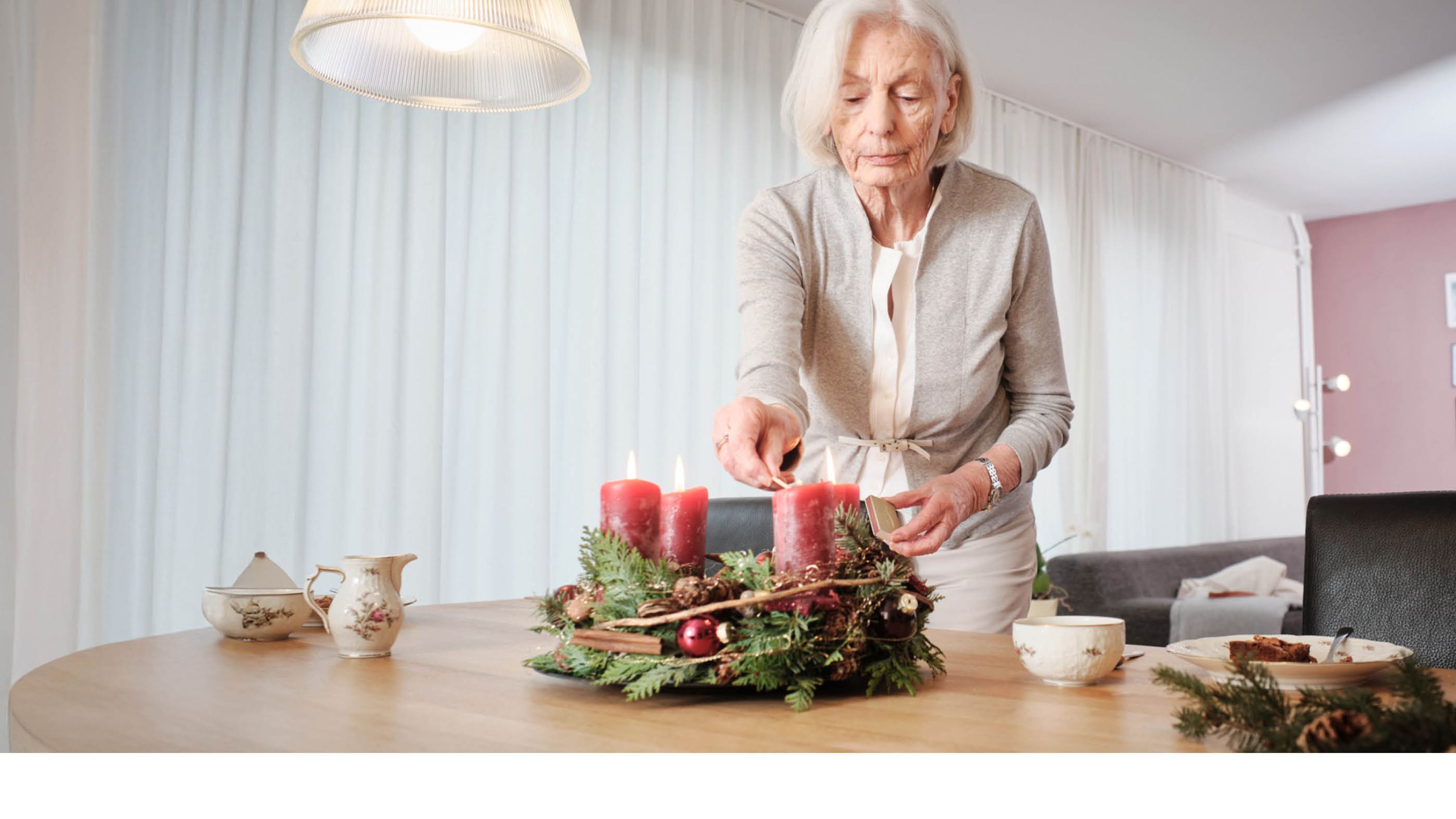 Eine Seniorin zündet eine Kerze des Adventskranzes an.